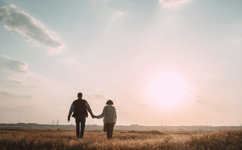 couple holding hands while walking on grass field during daytime